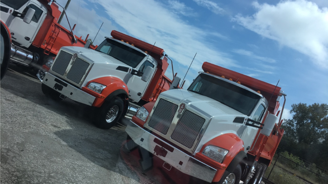 Three white semi-trucks parked inside a garage, next to support columns.