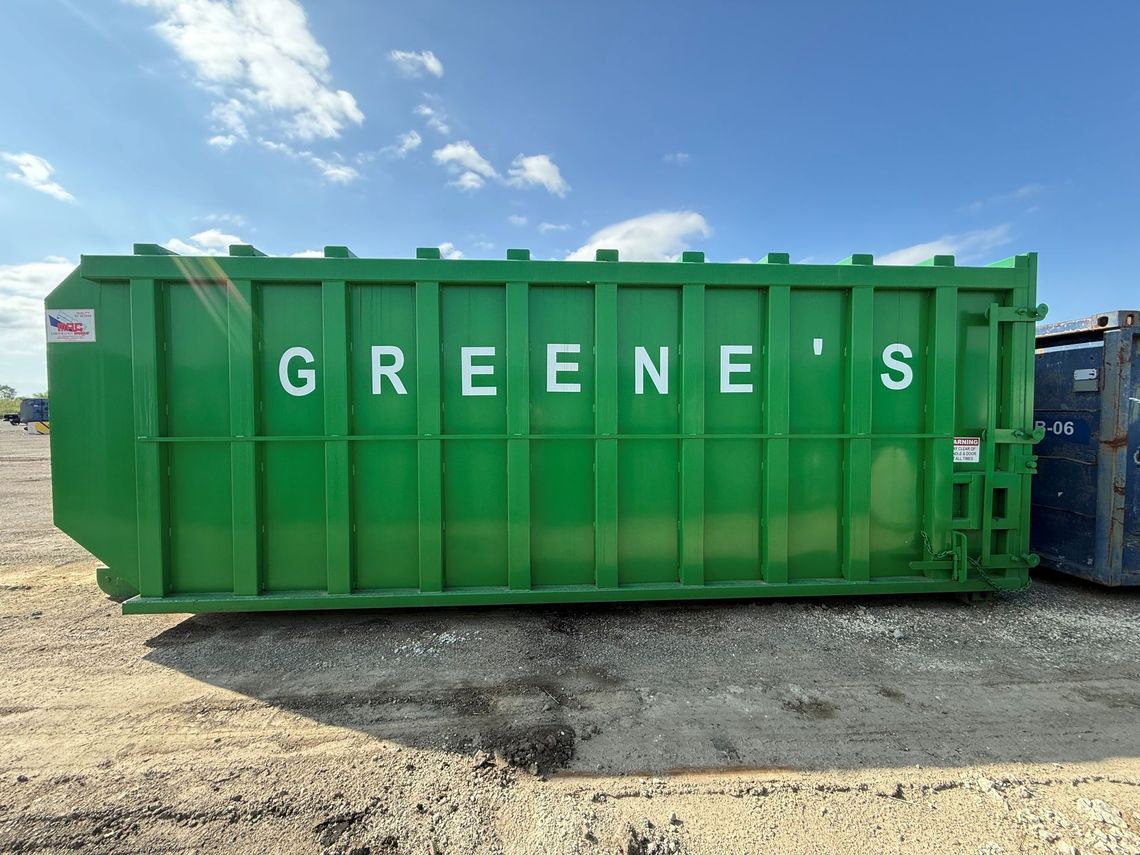 Red and green dumpsters on wheels sit side-by-side outdoors, with a backdrop of trees and a car.