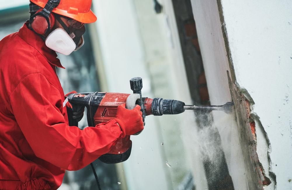 A Man is Using a Hammer Drill to Drill a Hole in a Wall — Husky Demolition In Maitland, NSW