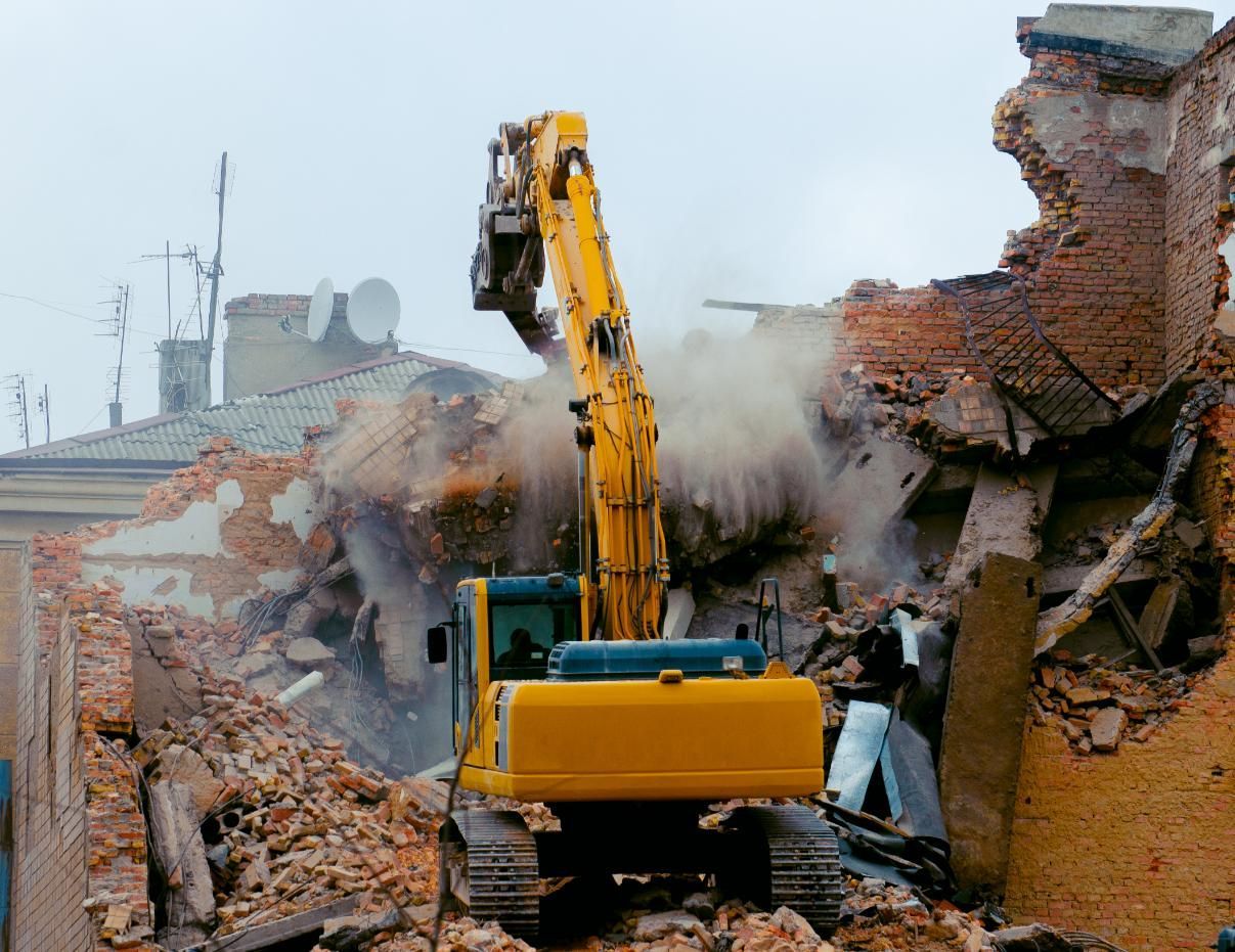 A Yellow Excavator is Demolishing a Brick Building — Husky Demolition In Forster, NSW