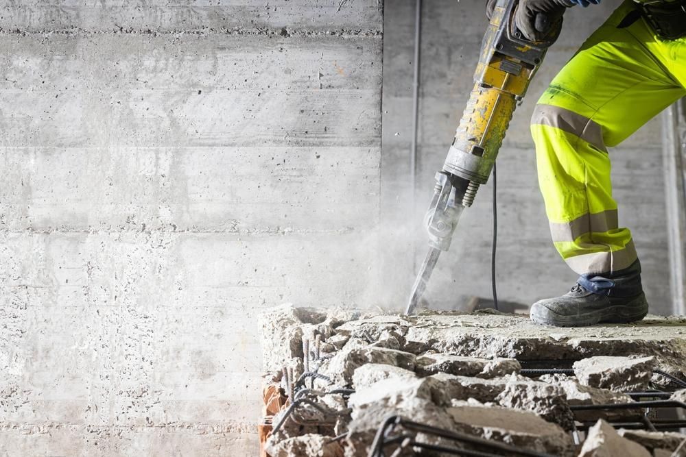 A Construction Worker is Using a Hammer to Break a Concrete Wall — Husky Demolition In Merewether, NSW