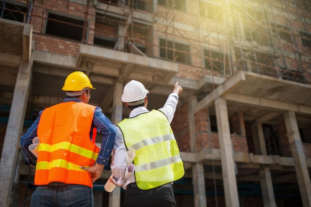 Two Construction Workers Are Standing in Front of a Building Under Construction — Husky Demolition In Port Stephens, NSW