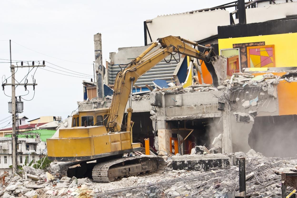 A Large Yellow Excavator is Demolishing a Building — Husky Demolition In Raymond Terrace, NSW