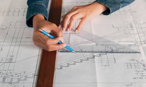 A person is using a ruler and pencil to draw a staircase on a blueprint.
