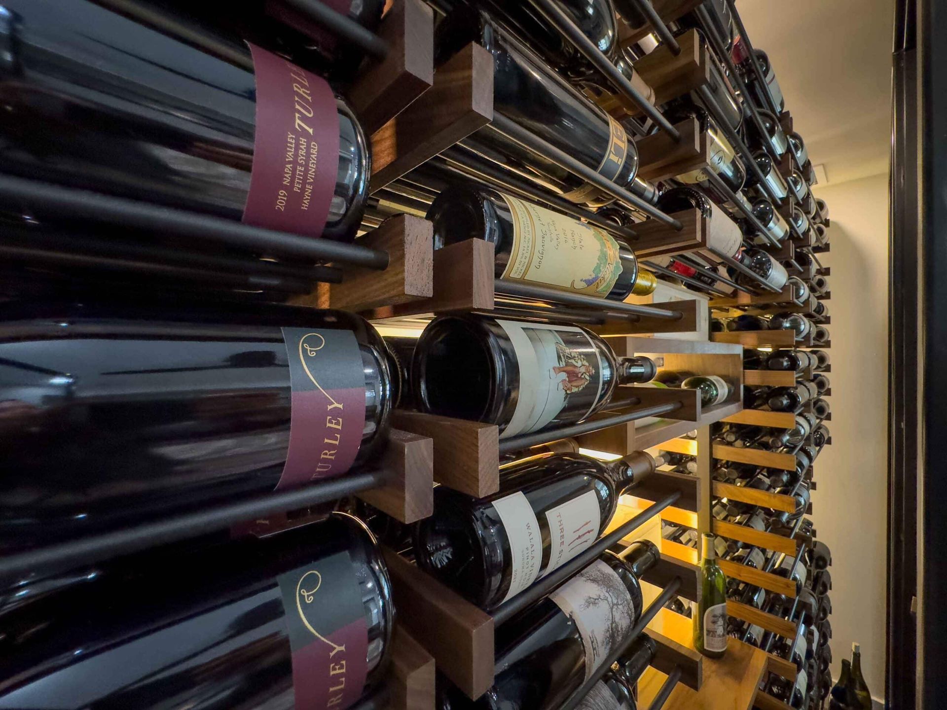 Rows of wine bottles stored horizontally in a cellar rack, with dark labels and warm lighting.