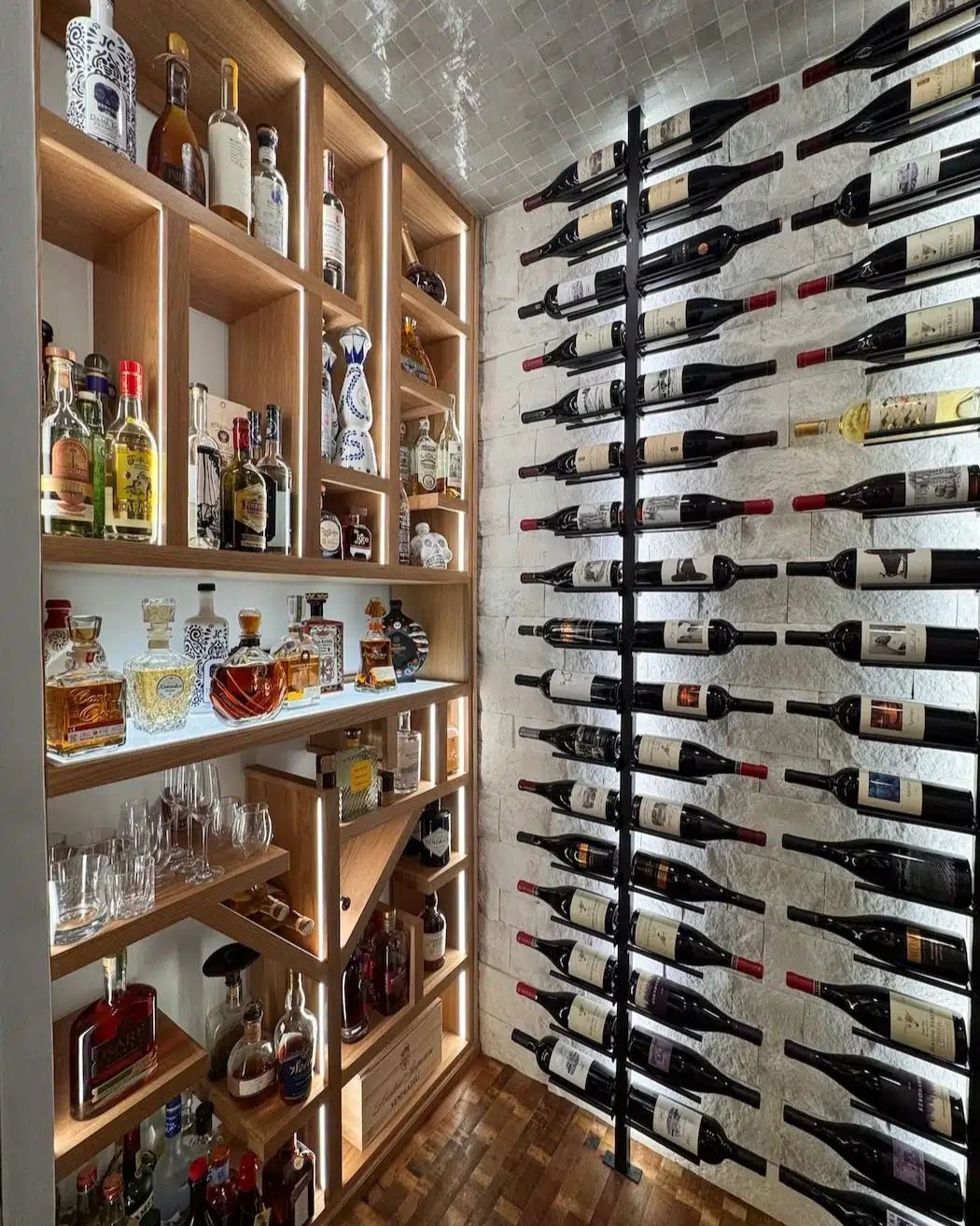 Wine cellar with wooden shelves of bottles and glasses, plus wall-mounted horizontal wine racks.