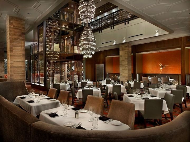 Elegant upscale restaurant dining room with white tablecloths, chandelier lights, and warm wood accents