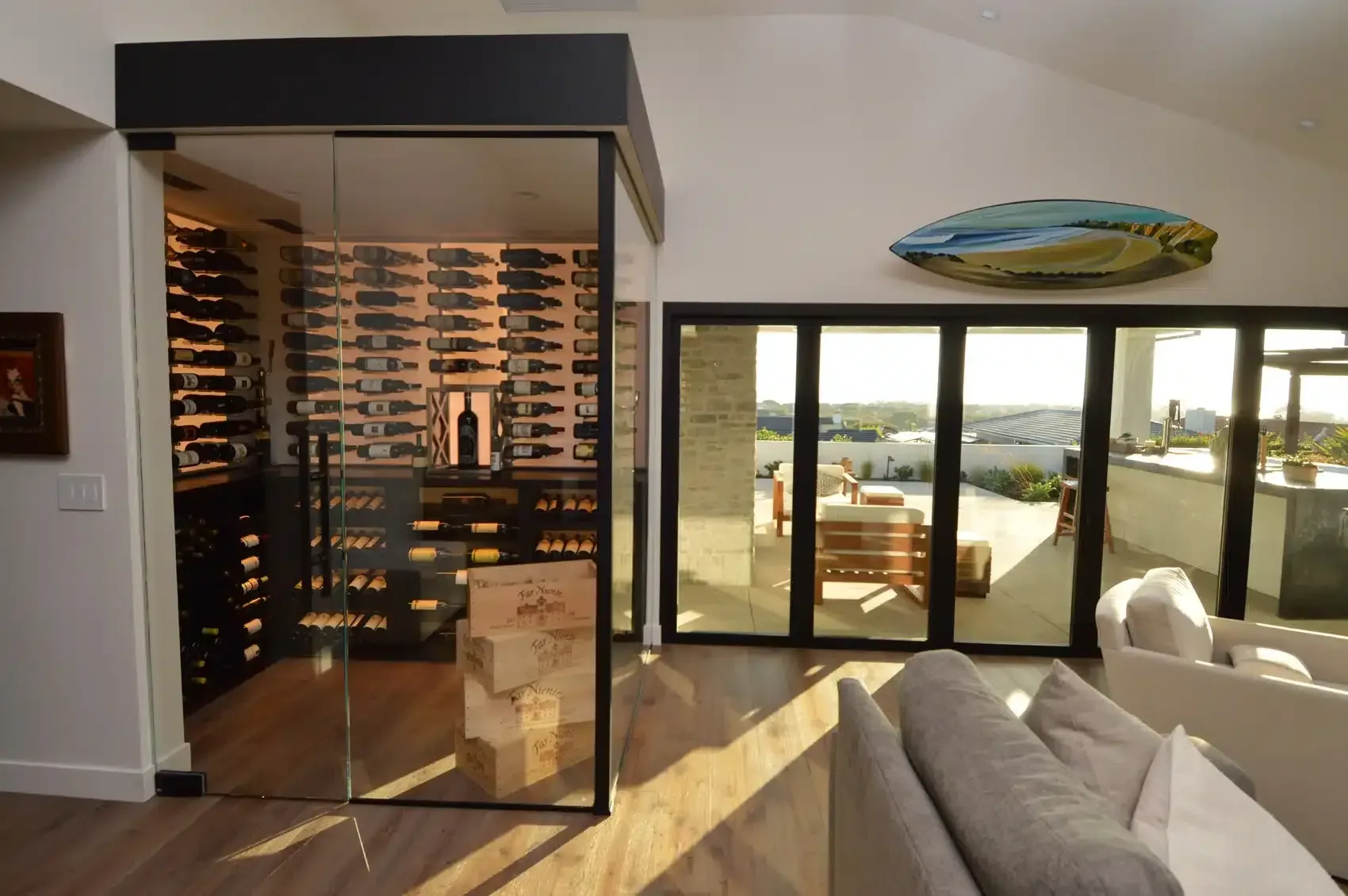 Living room with glass wine cellar, sofa, and sliding doors to a sunlit patio and water view