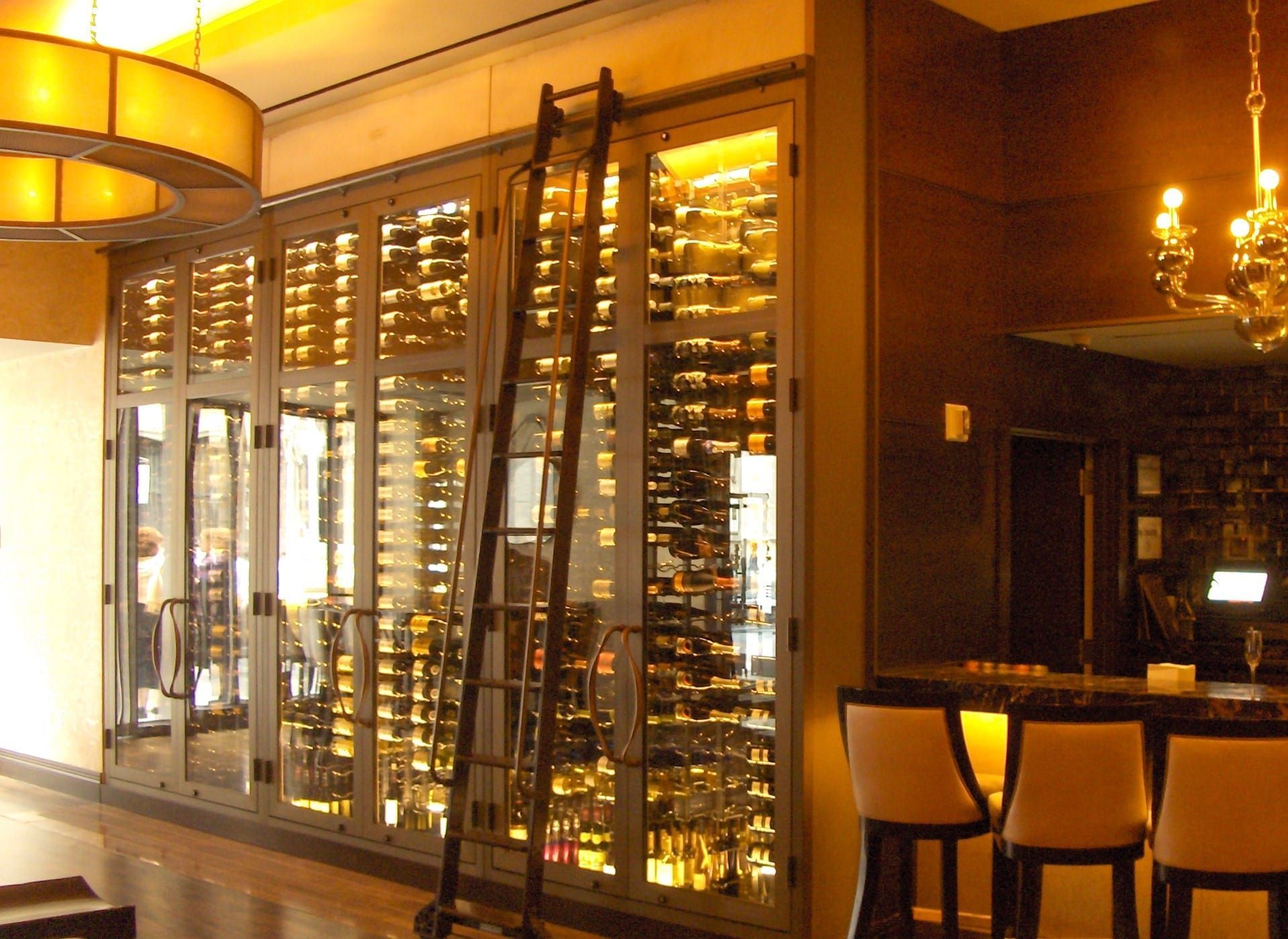 Warmly lit restaurant or wine bar with glass wine storage wall and small table seating