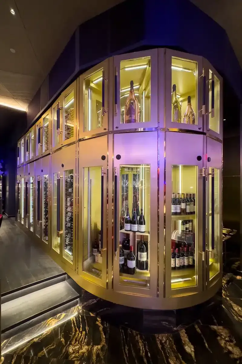 Purple-lit glass display cabinets with wine bottles in a sleek, curved interior hallway