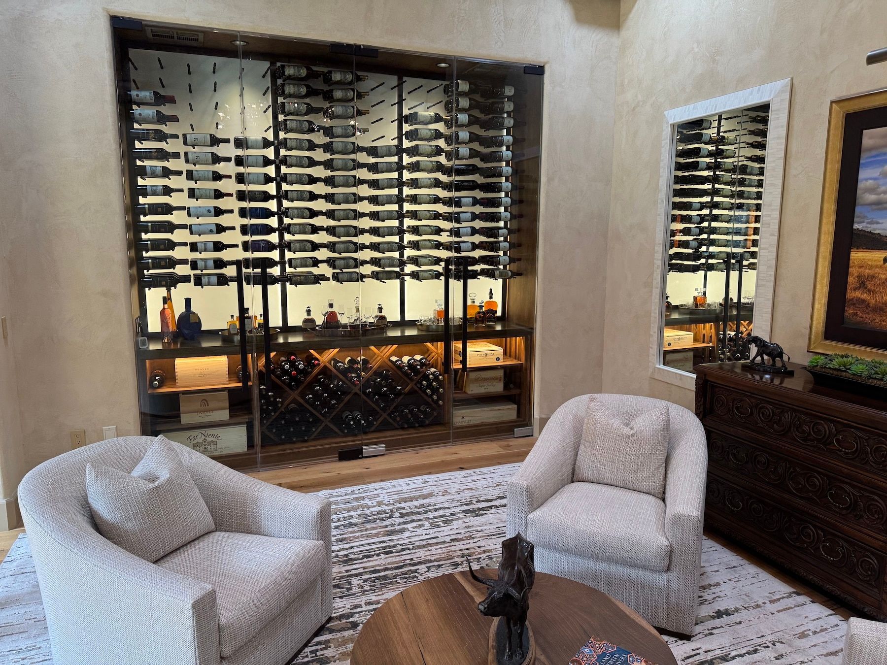 Modern lounge with two white chairs, coffee table, wine display, and framed wall art.