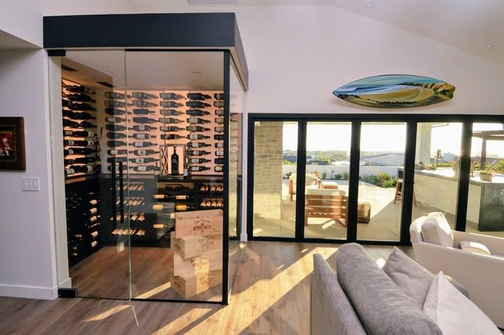 Modern living room with wine display, sofa, and large glass doors opening to a balcony with ocean view