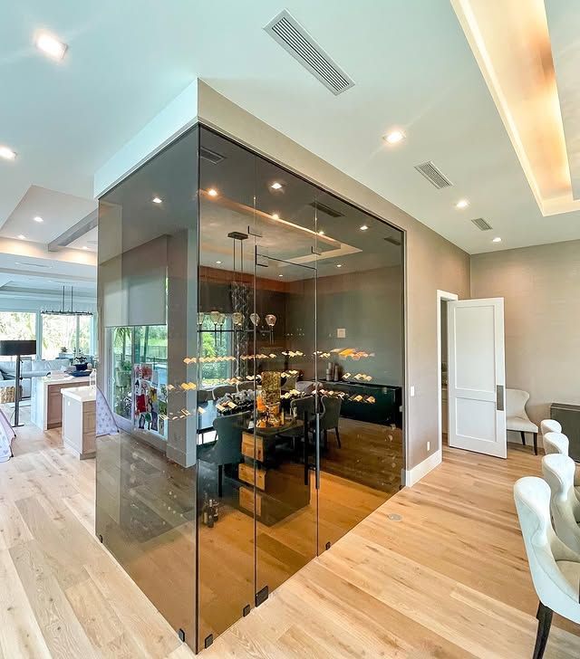 Modern open-concept dining area with glass wine room, light wood floors, and sleek white chairs