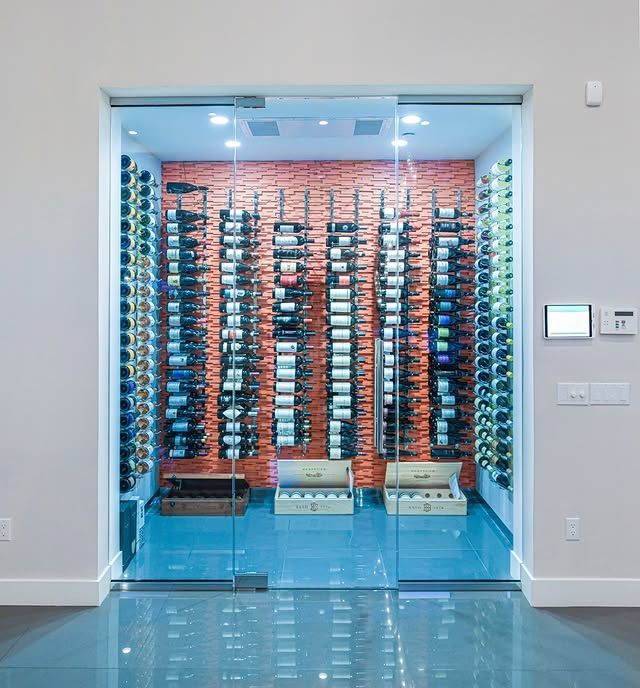 Glass-front wine cellar with rows of bottles behind blue-tinted doors in a modern interior