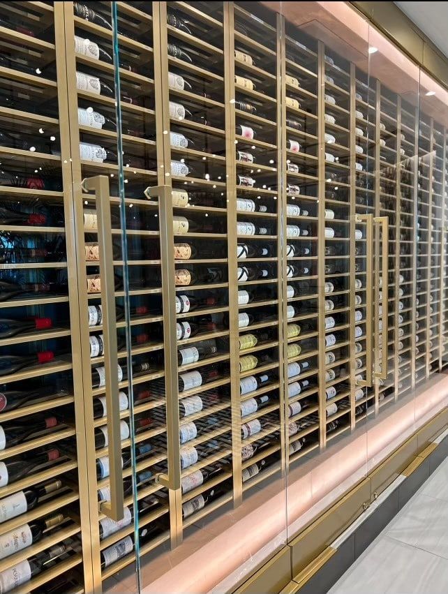 Rows of wine bottles stored on wooden racks behind glass in a shop or cellar.