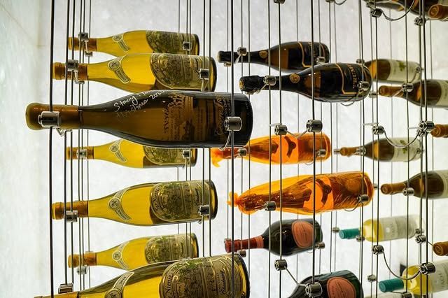 Wine bottles displayed horizontally in a wall-mounted rack, with some yellow, dark, and orange bottles visible.