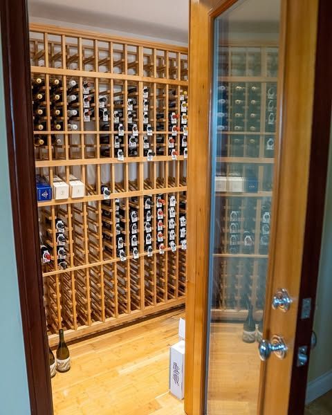Wine cellar with wooden racks full of bottles, viewed through an open glass door