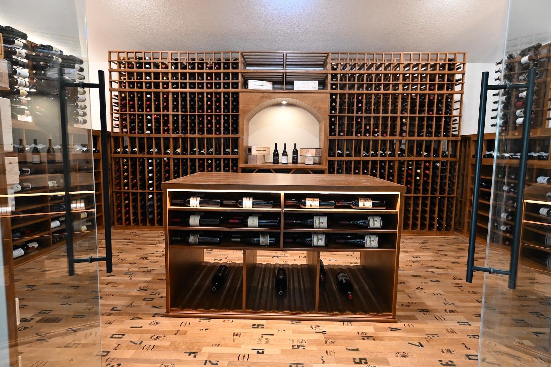 Wine cellar with wooden racks, central display table, and bottles on shelves in a warm-lit room
