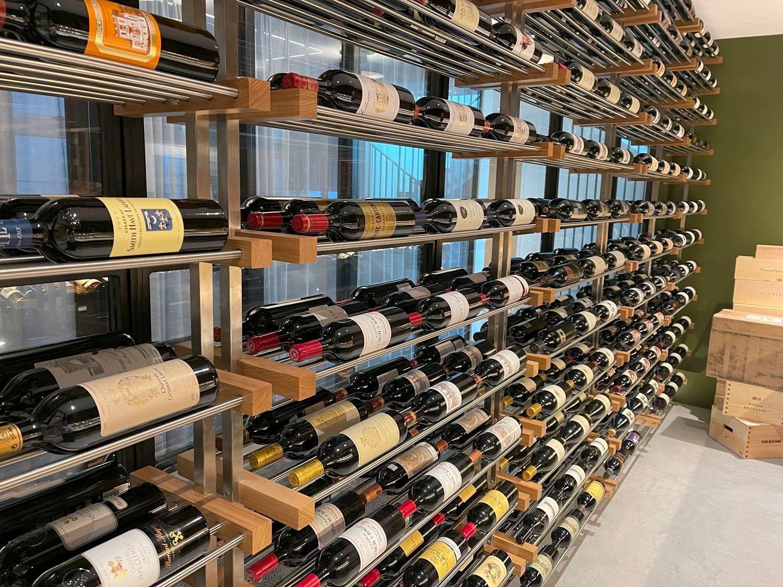 Rows of wine bottles on wooden shelves in a store cellar, with a few cardboard boxes nearby.