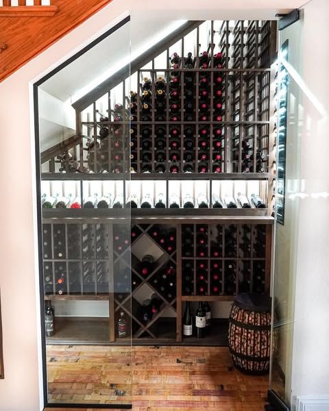 Built-in under-stair wine cellar with glass doors, red wine bottles, and wooden floor