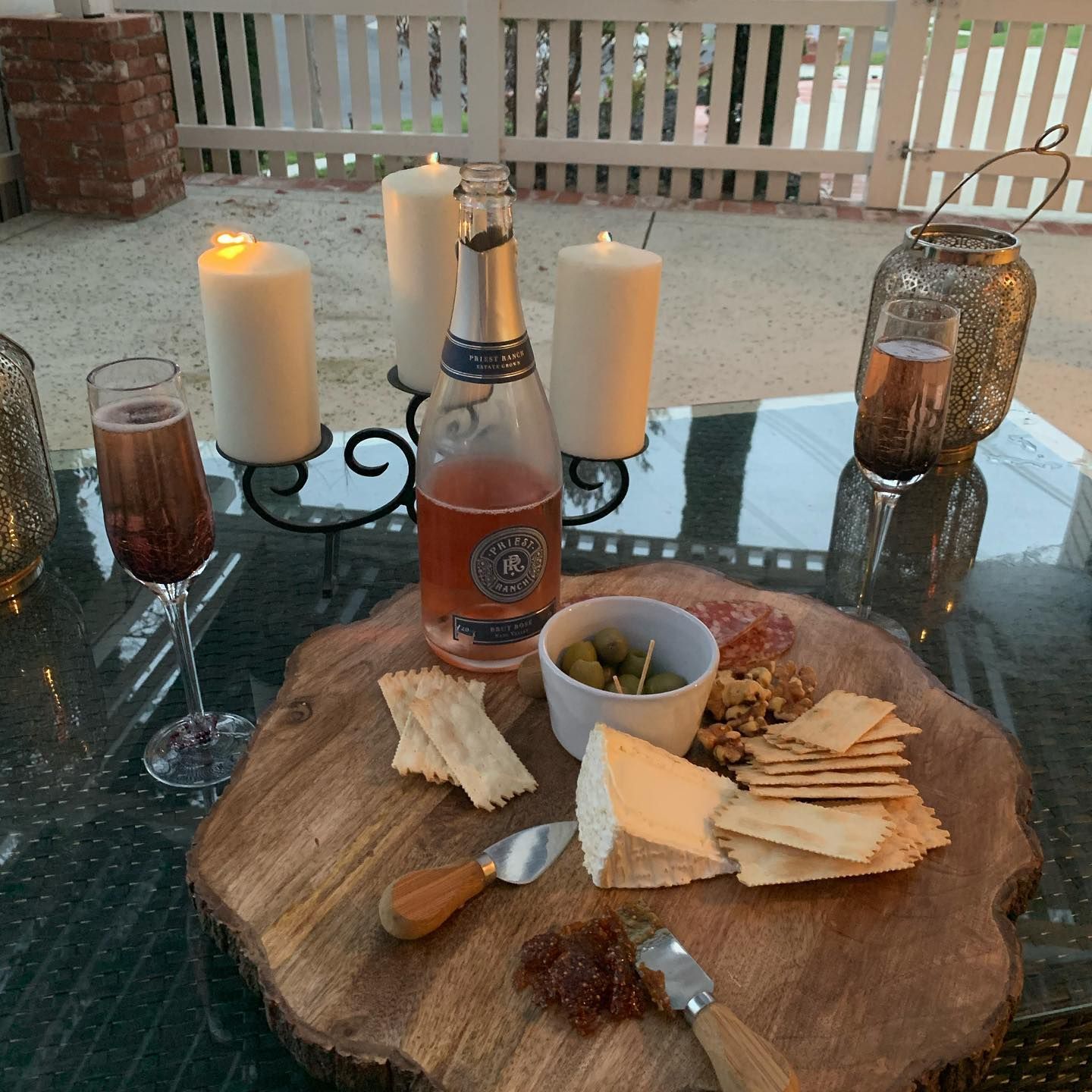 Outdoor charcuterie board with crackers, cheese, dip, and a drink by lit candles on a table