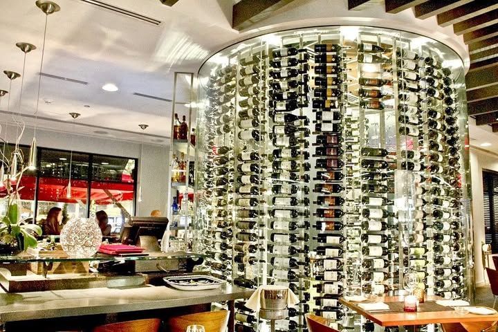 Modern restaurant interior with a tall wine bottle display and diners seated nearby
