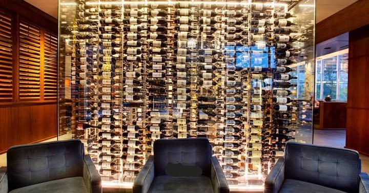 Three black chairs facing a wall of stacked wine bottles in a warmly lit wine cellar