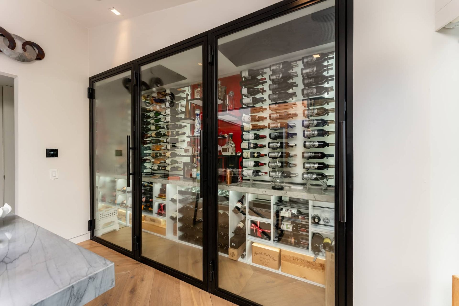 Glass-front wine display cabinet in a modern room, filled with wine bottles and boxes