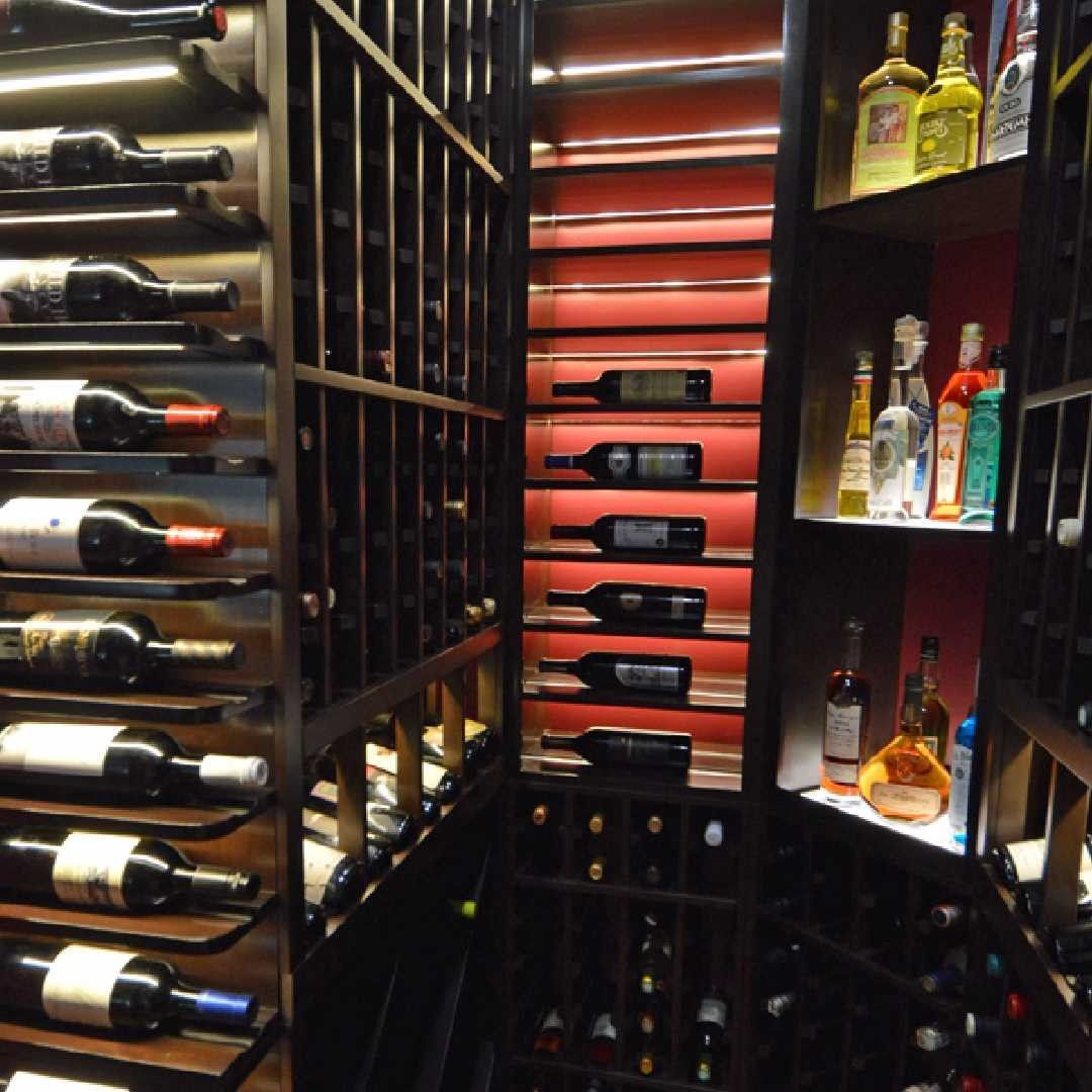 Wine cellar with rows of wine bottles on racks and shelves in a narrow storage room.