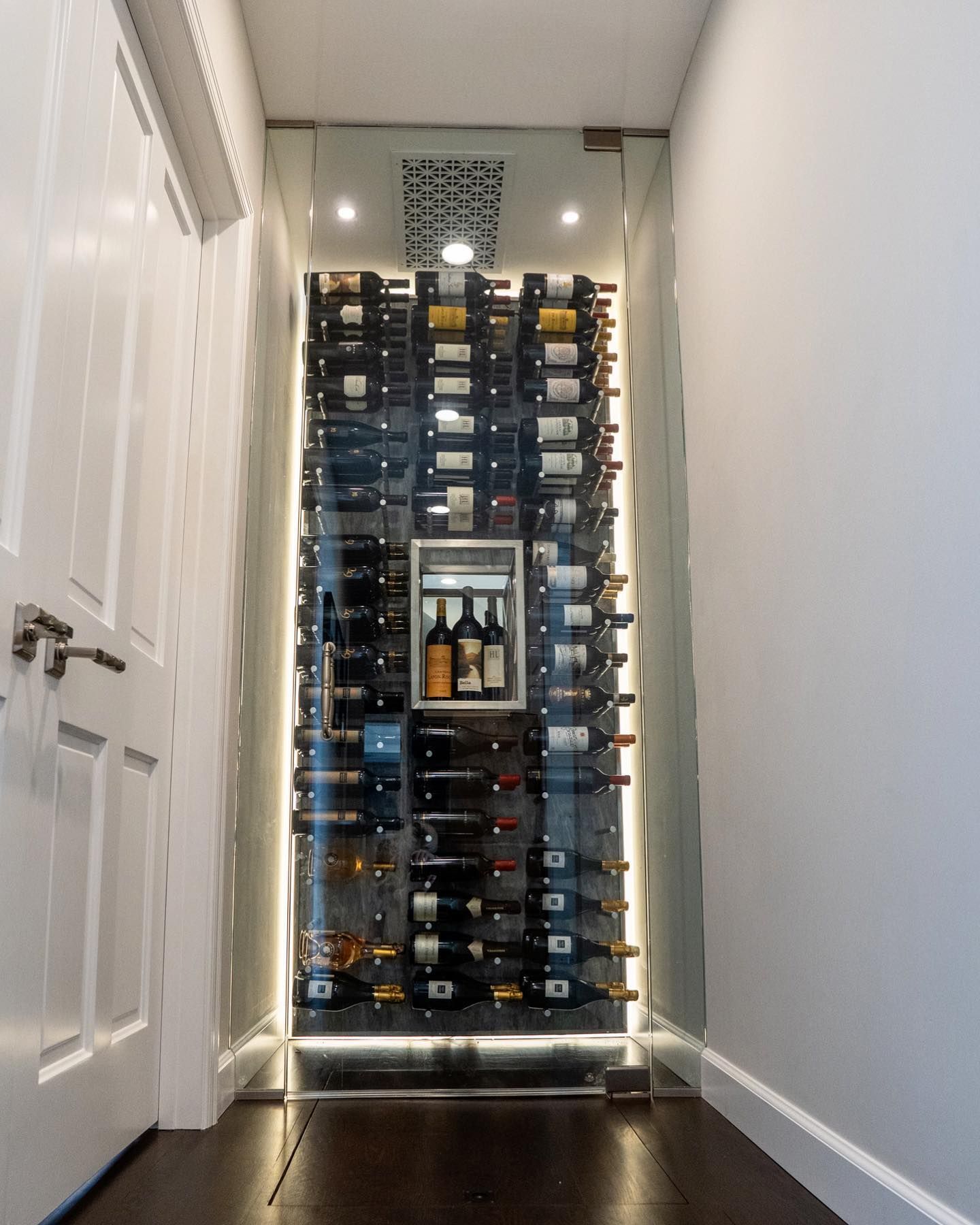 Tall wine rack with many bottles in a narrow hallway, lit by warm string lights.
