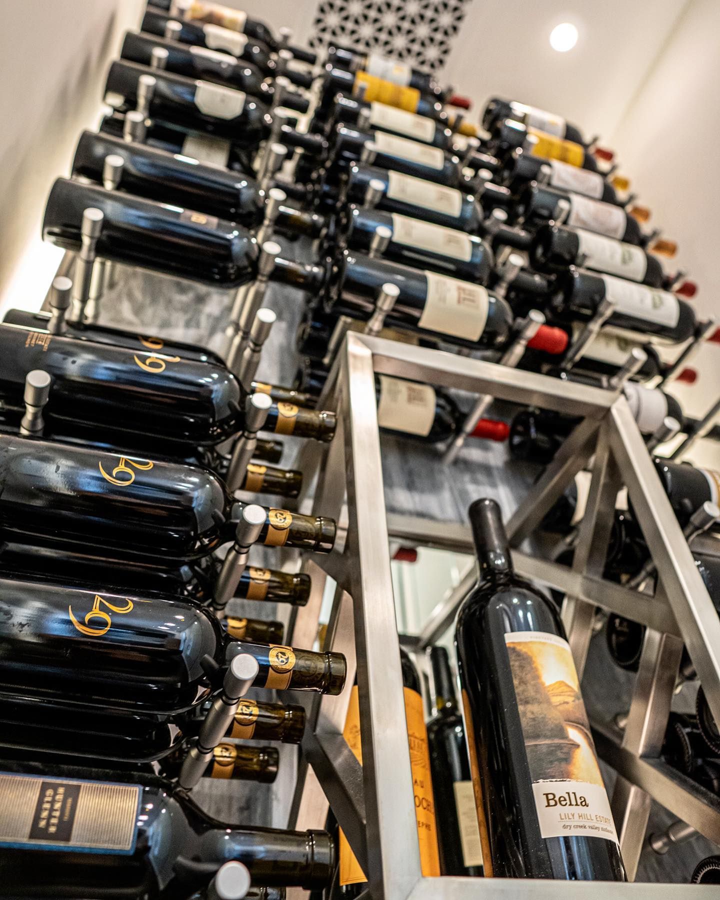 Rows of wine bottles stacked on a metal rack in a cellar, viewed at an angle.