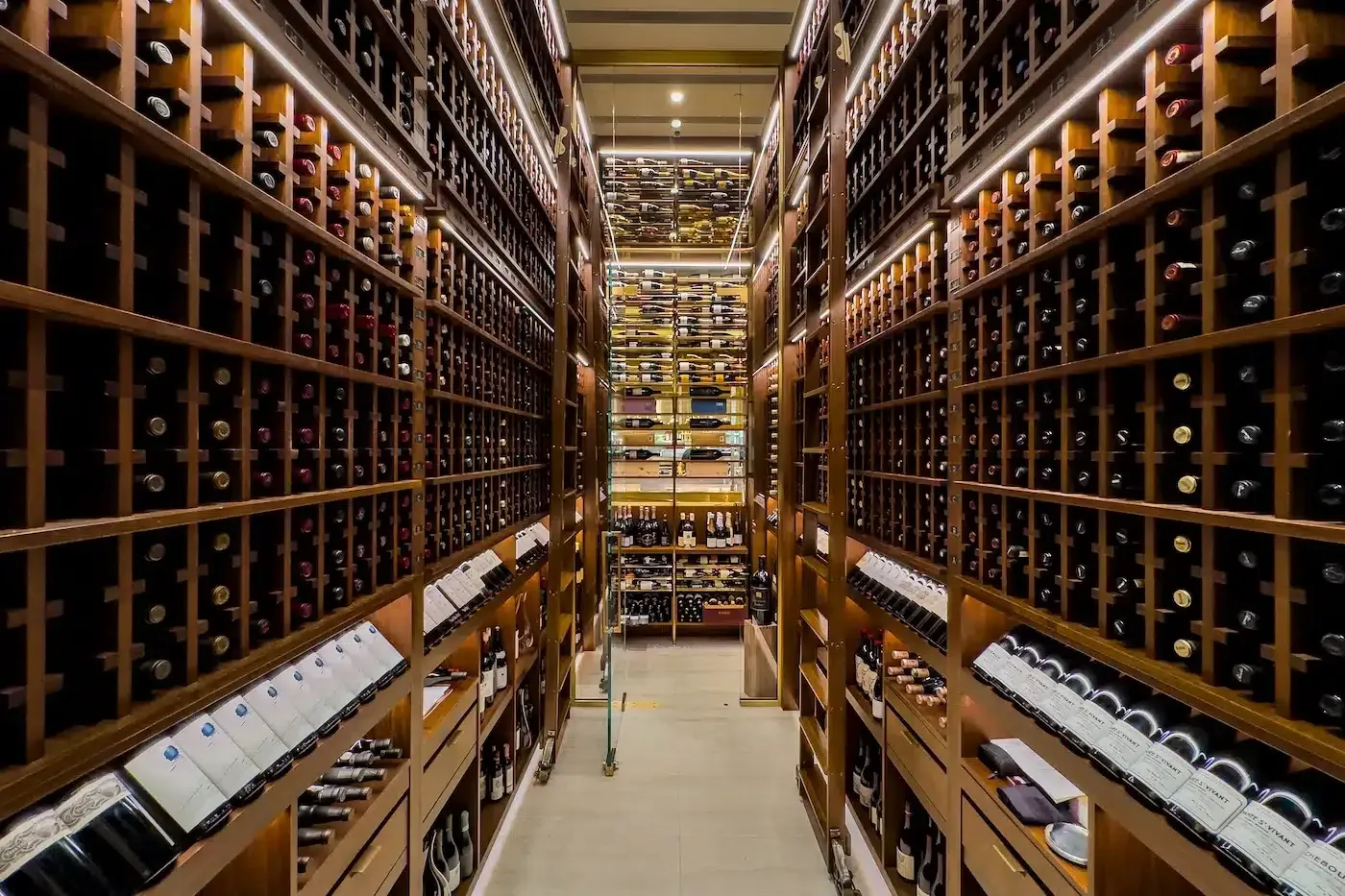 A wine cellar aisle with floor-to-ceiling wooden racks filled with bottles on both sides.