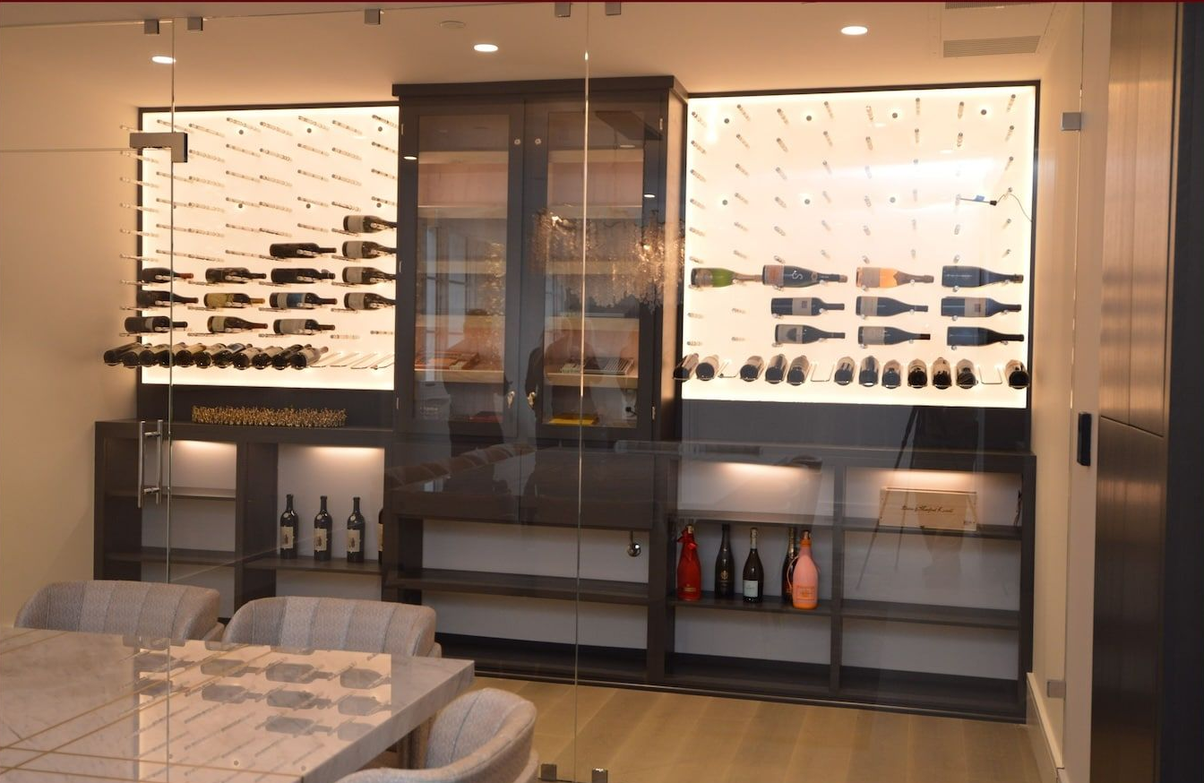 Modern lounge with illuminated glass wine cabinets, shelves, and a dining table in warm lighting