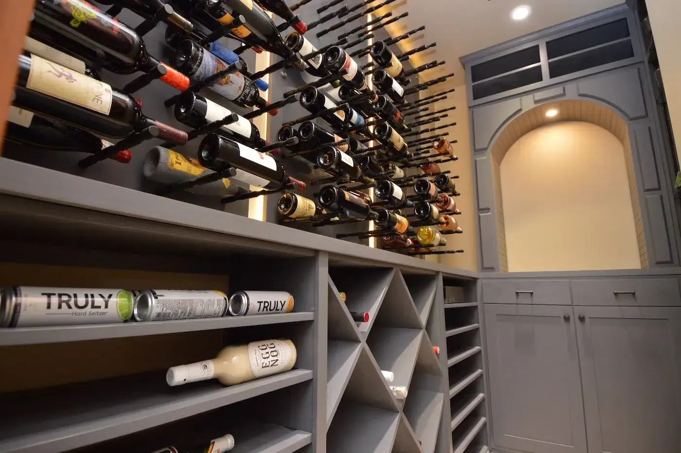 Wine cellar with bottle racks, shelves, and a gray arched door in warm lighting