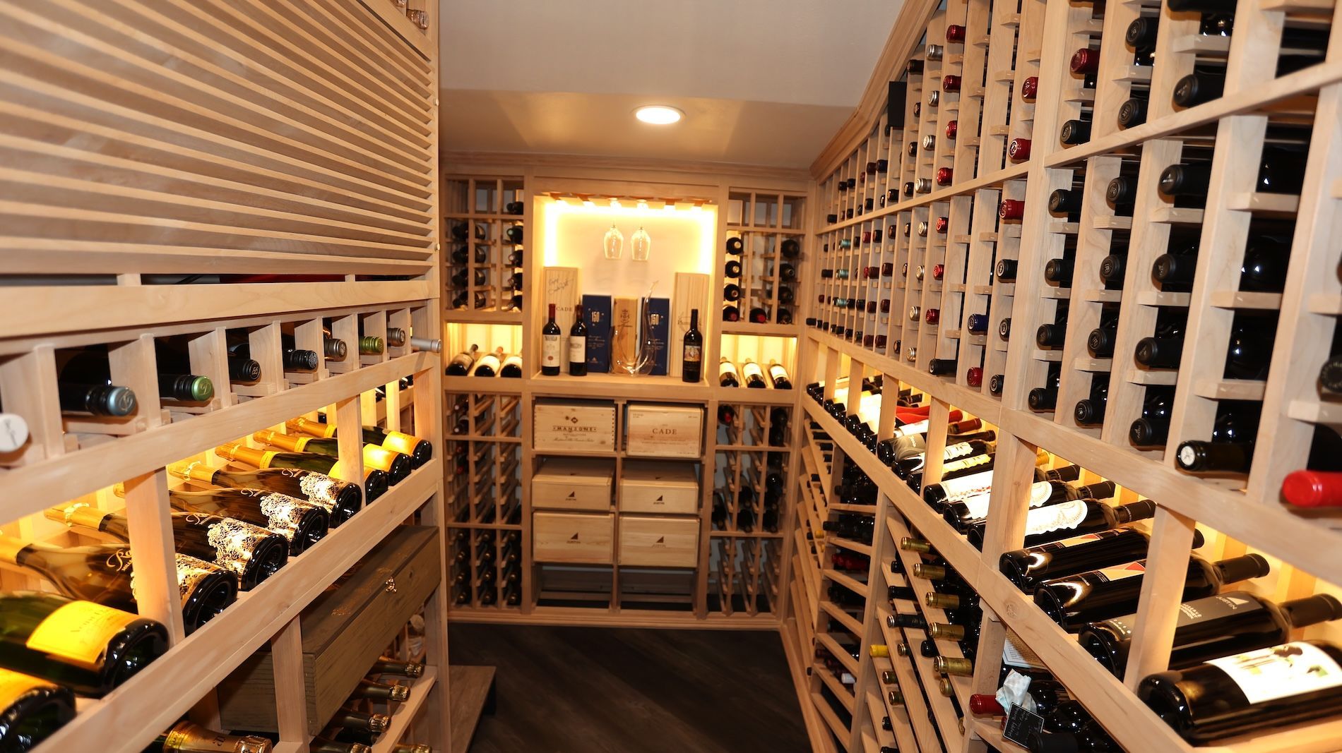 Warm-lit wine cellar with floor-to-ceiling shelves of bottles and a central cabinet of storage drawers