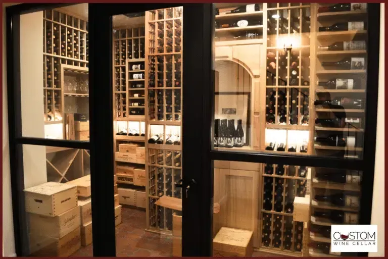 Glass wine cellar with rows of bottles on wooden racks and shelves in a warmly lit room