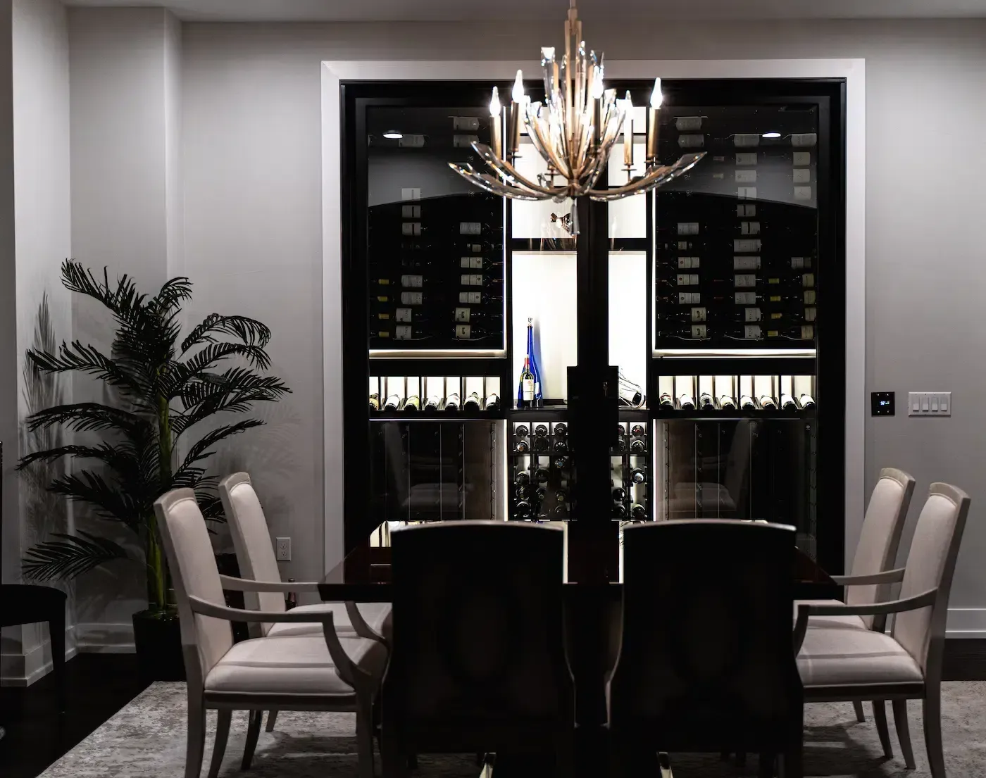 Elegant dining room with chandelier, dark table, upholstered chairs, and wine display cabinets