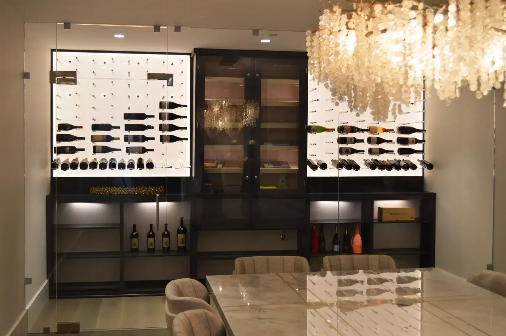 Modern dining room with wall wine displays, a chandelier, and a reflective glass table