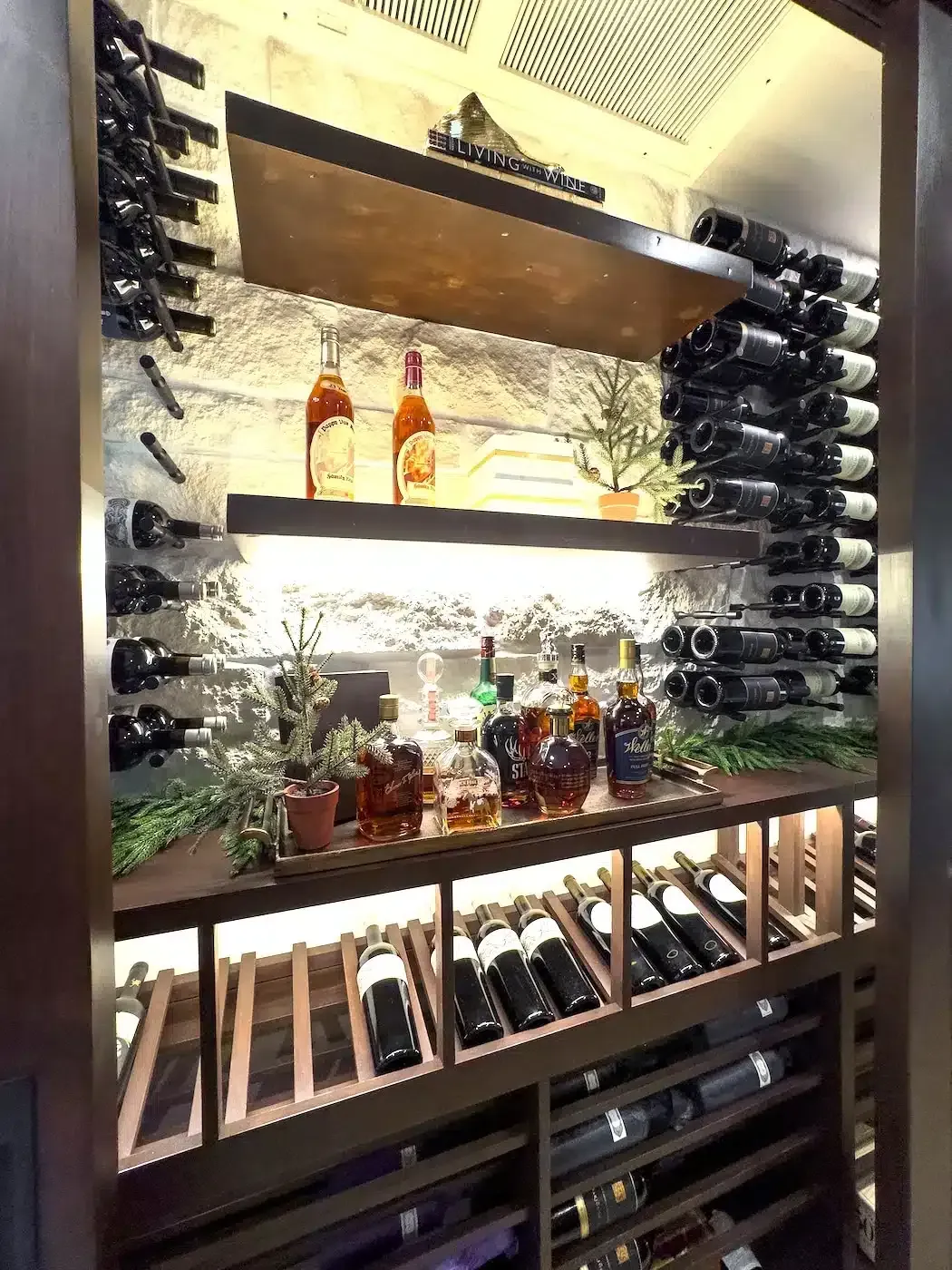 Wine display with bottles on shelves, backlit against a stone wall in a modern bar.