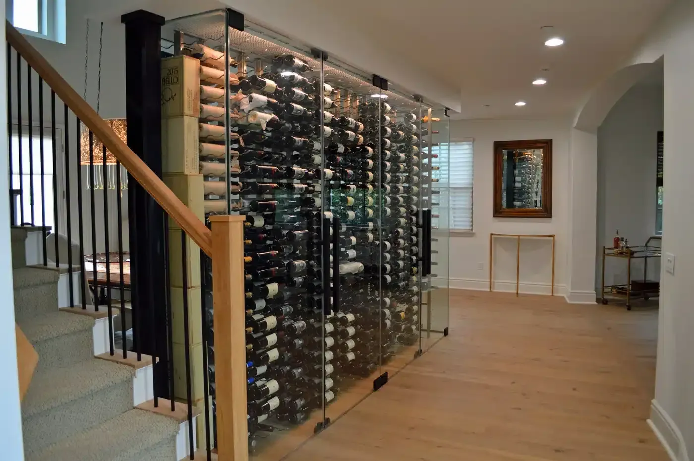 Wine cellar beside a staircase in a modern home, with floor-to-ceiling glass racks and wood flooring