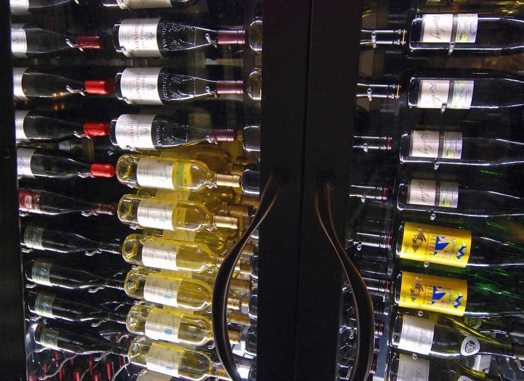 Wine bottles arranged in a glass-front refrigerator, including red, white, and sparkling wines.