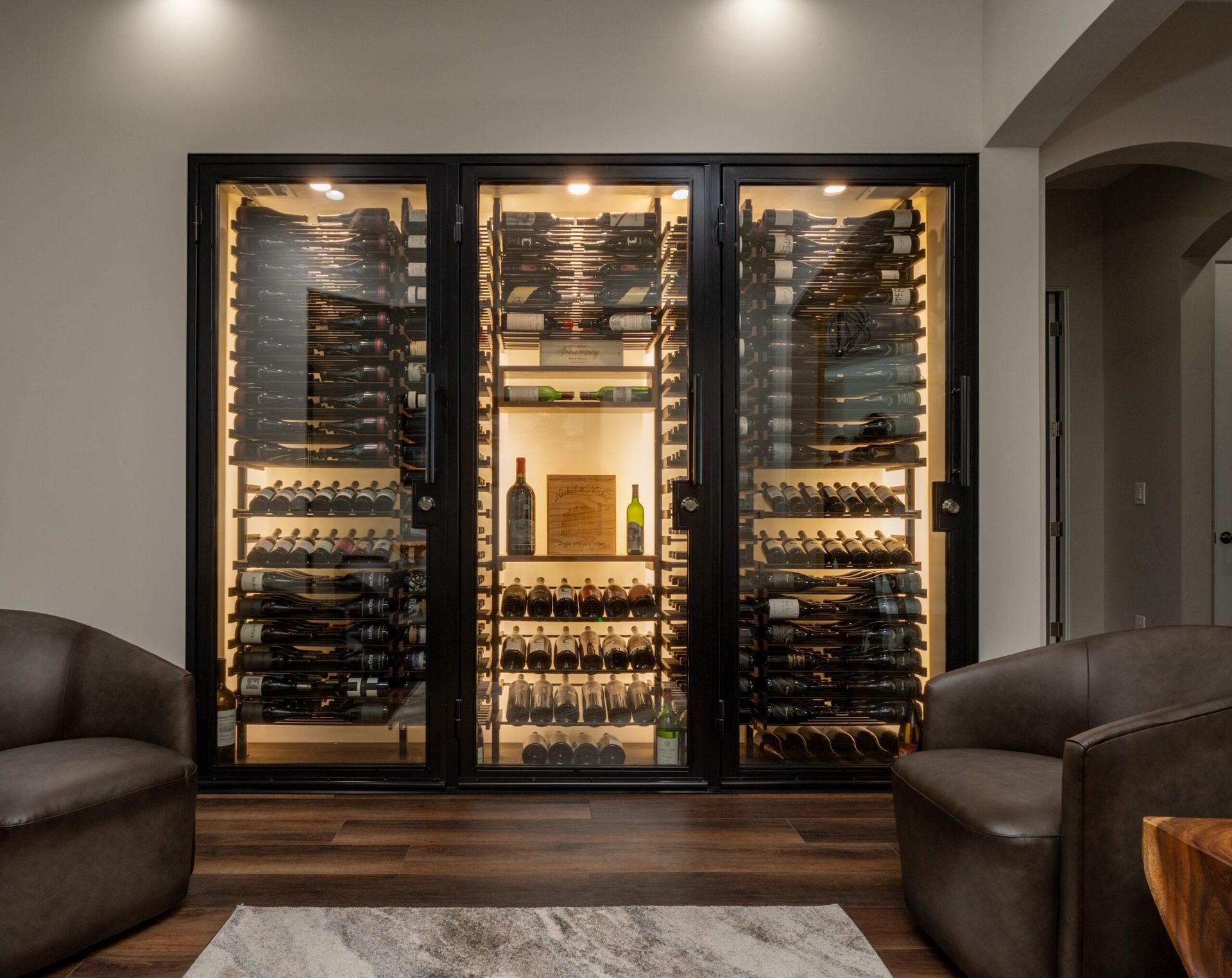 Built-in wine cellar with glass doors, warm lighting, and rows of wine bottles in a modern room