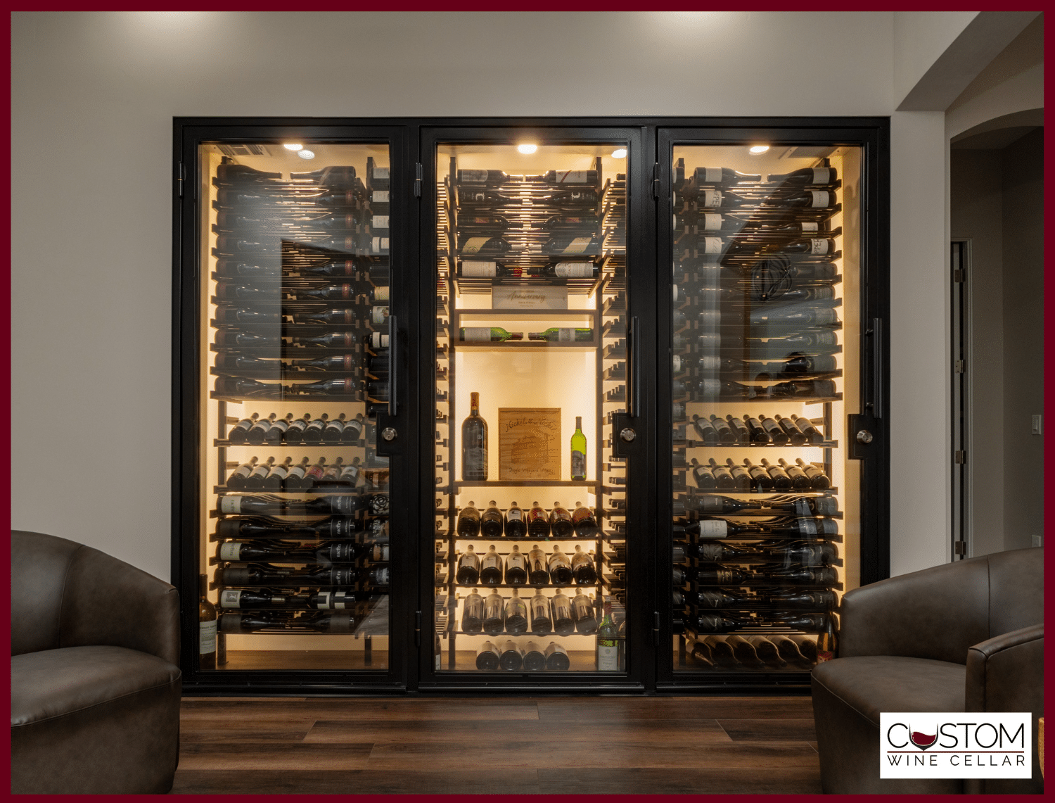 Built-in glass wine cellar with bottles and central display, framed by two armchairs in a modern room