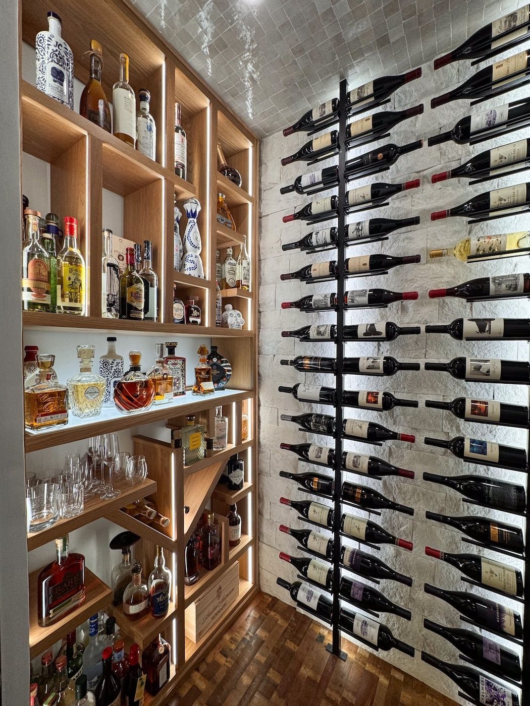 Wooden wine rack and glass shelves in a narrow home wine cellar with bottles stored horizontally on the wall
