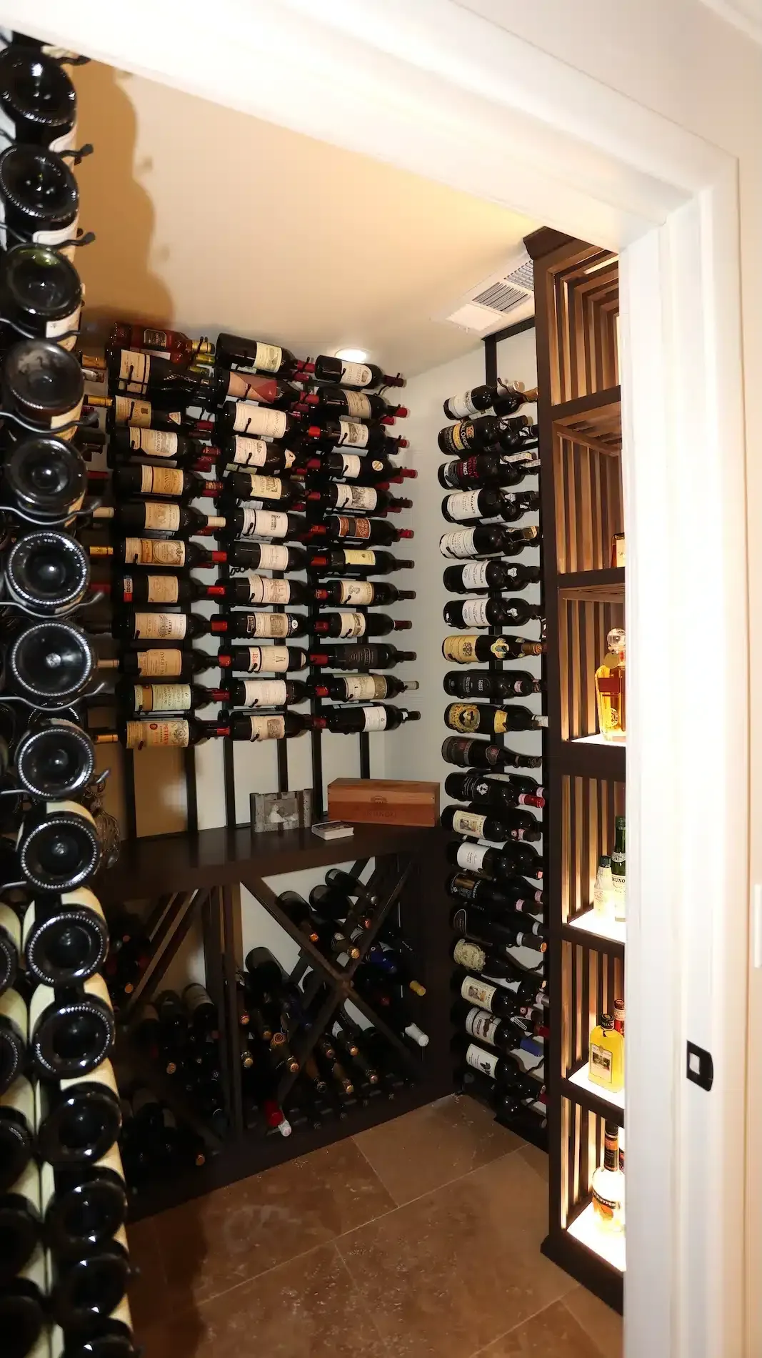 Small wine cellar with floor-to-ceiling bottle racks and many wine bottles stacked on shelves.