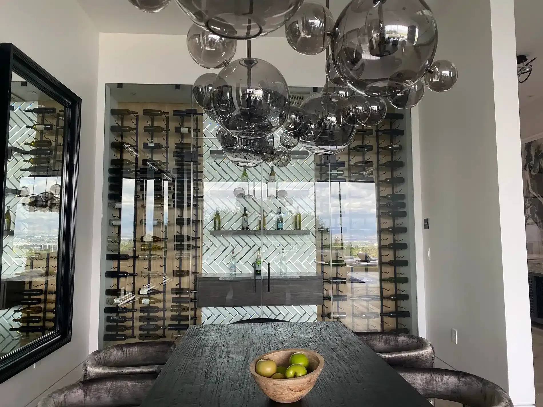 Modern dining room with wine wall, glass pendant lights, and a bowl of fruit on the table