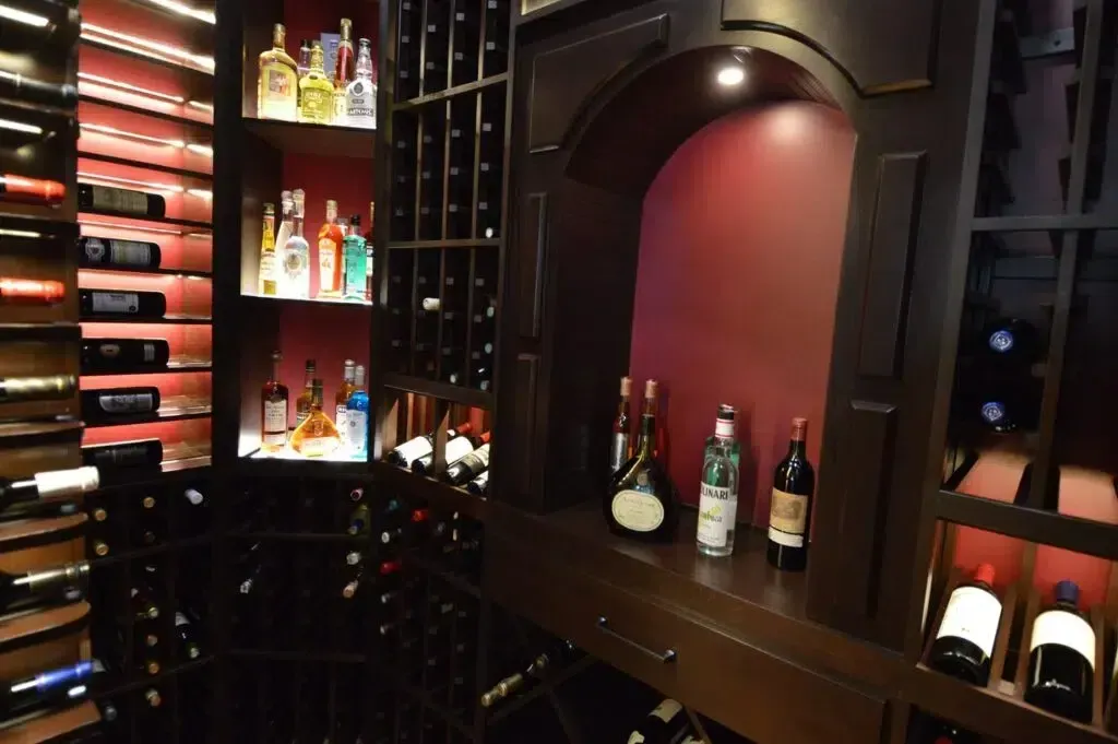 Dimly lit wine cellar with bottles on shelves and in cubbies against dark wood walls