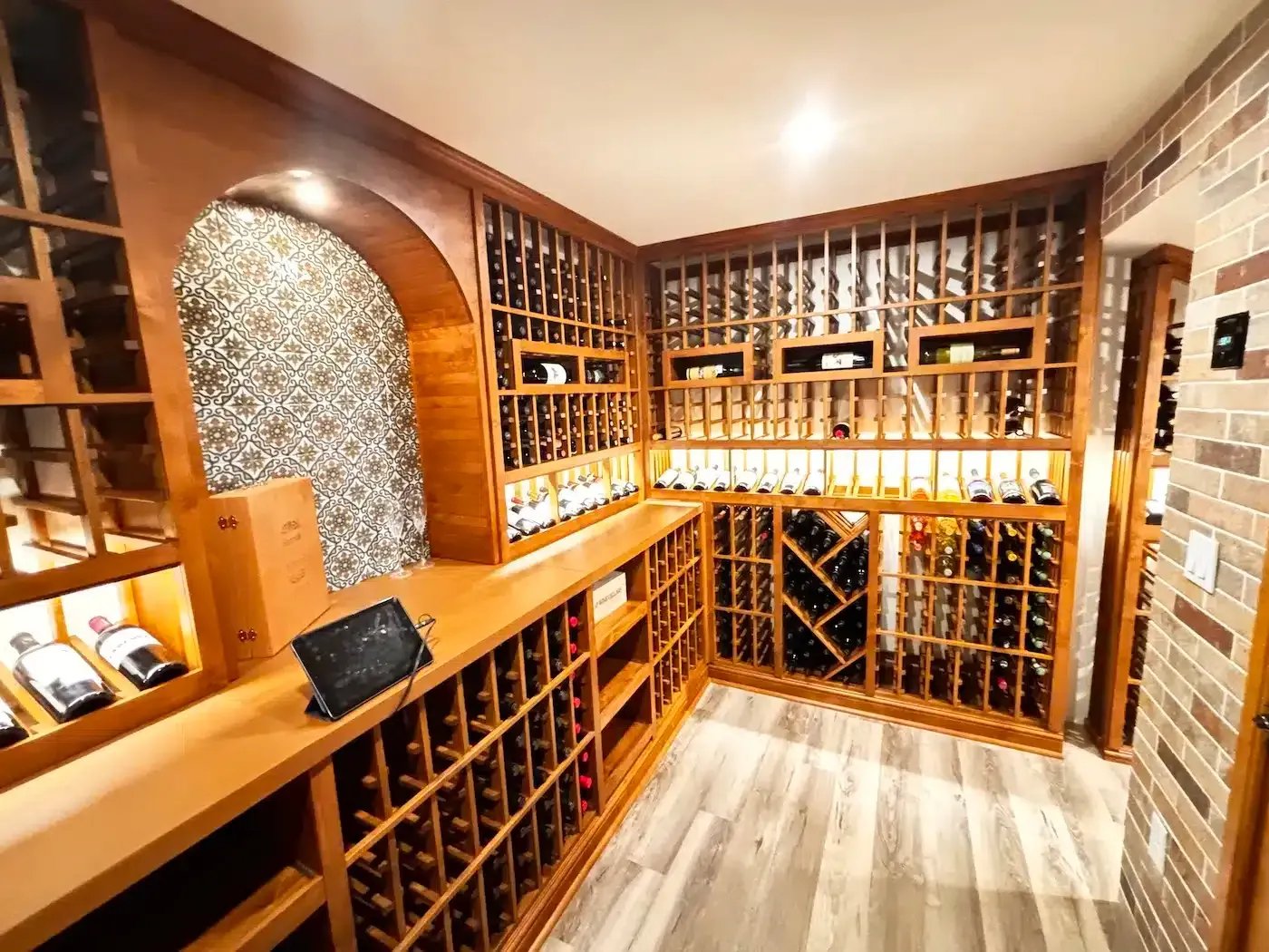 Wood-paneled wine cellar with wooden racks, bottles, and stone accent walls under warm lighting
