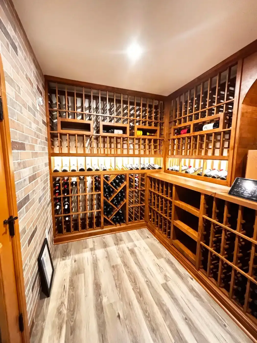 Empty wine cellar with wooden racks, stone walls, and a warm ceiling light.