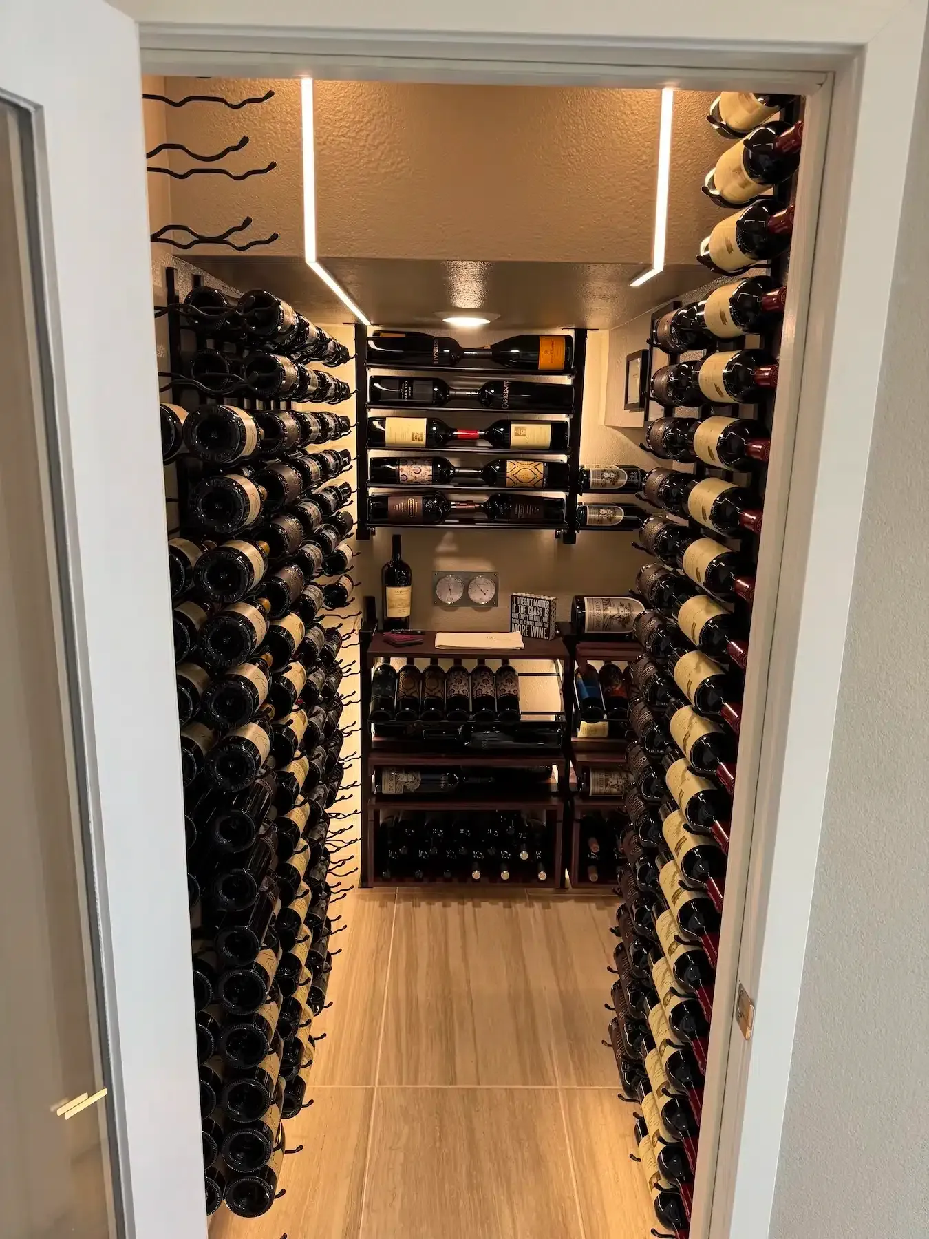 Small wine cellar with floor-to-ceiling bottle racks and shelves stocked with wine bottles and decor